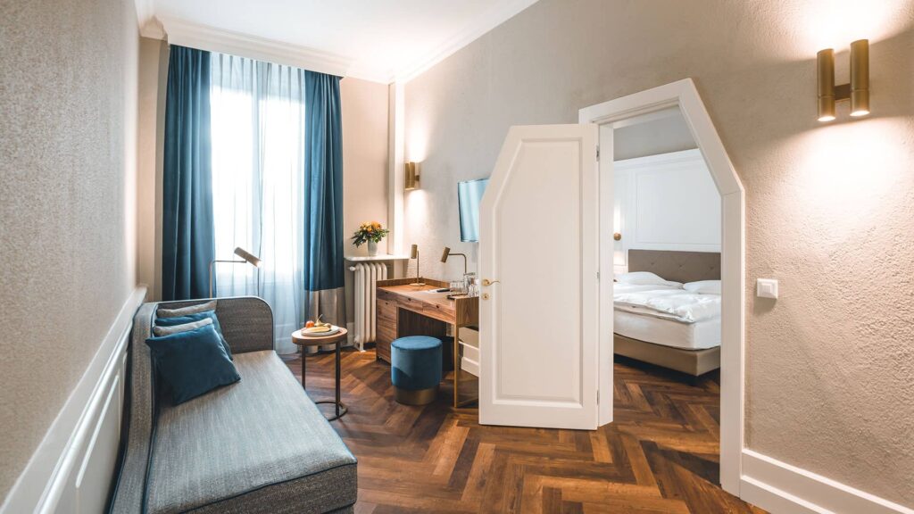 Erleben Sie die unaufdringlich royale Atmosphäre: Wohnraum mit Récamière, und begehbarem Kleiderschrank, elegantes Schlafzimmer und durchdachte Ambientebeleuchtung.